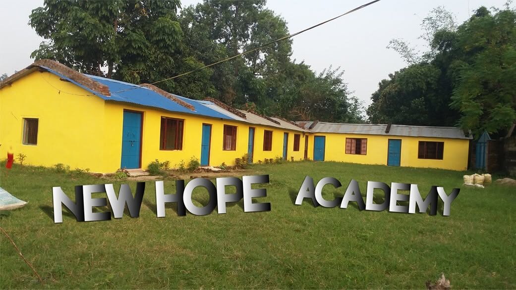 The marigold-yellow school building with New Hope Academy painted across the wall