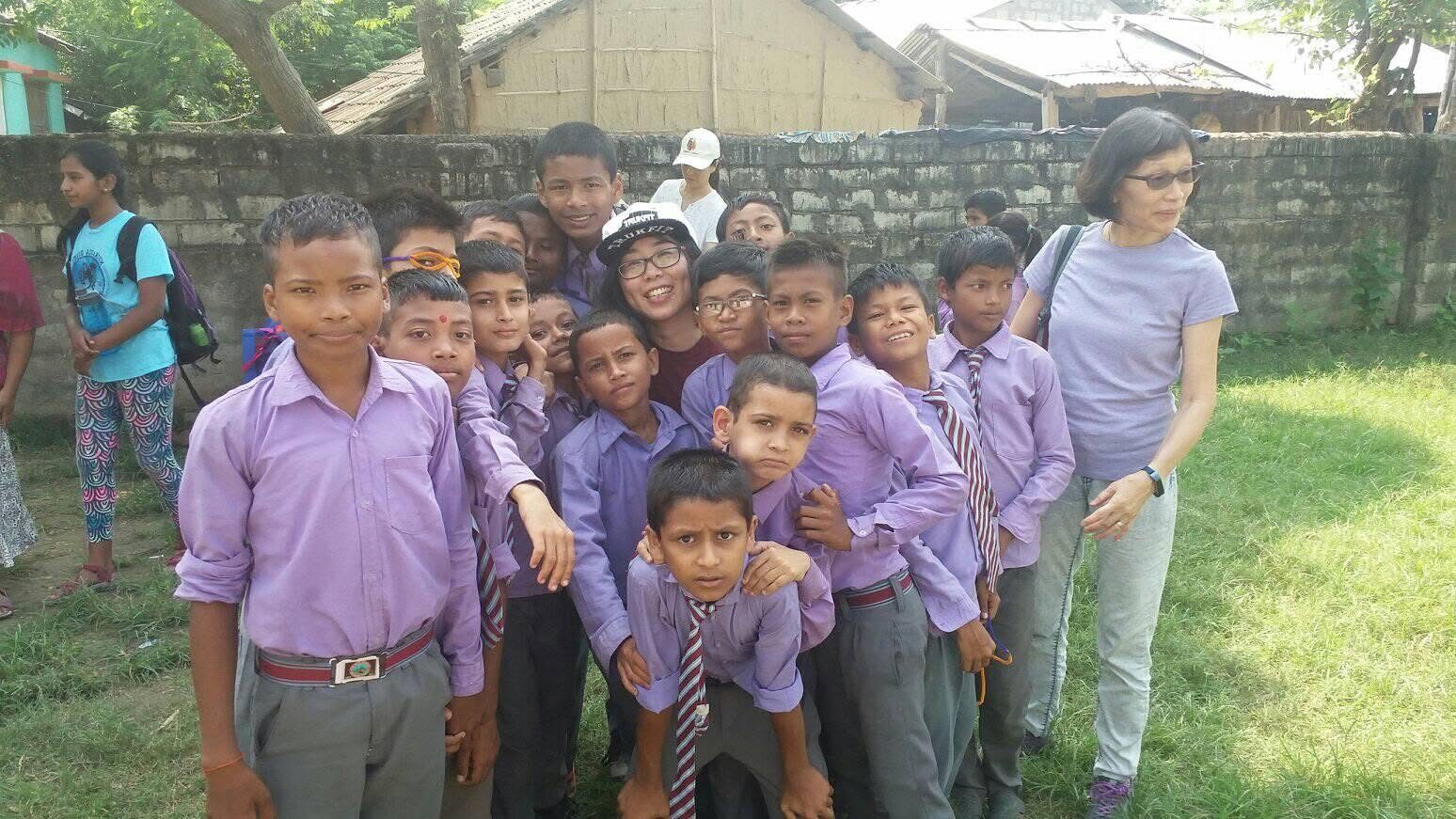 Students in purple shirts crowding happily around two visitors for a photo
