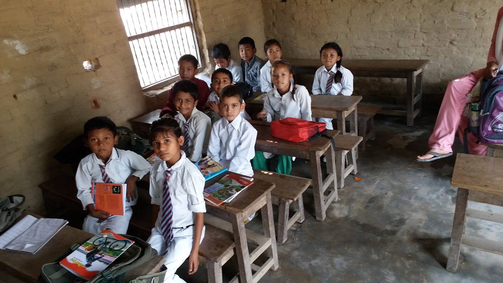 Students at their wooden desks inside the classroom, looking up from their books