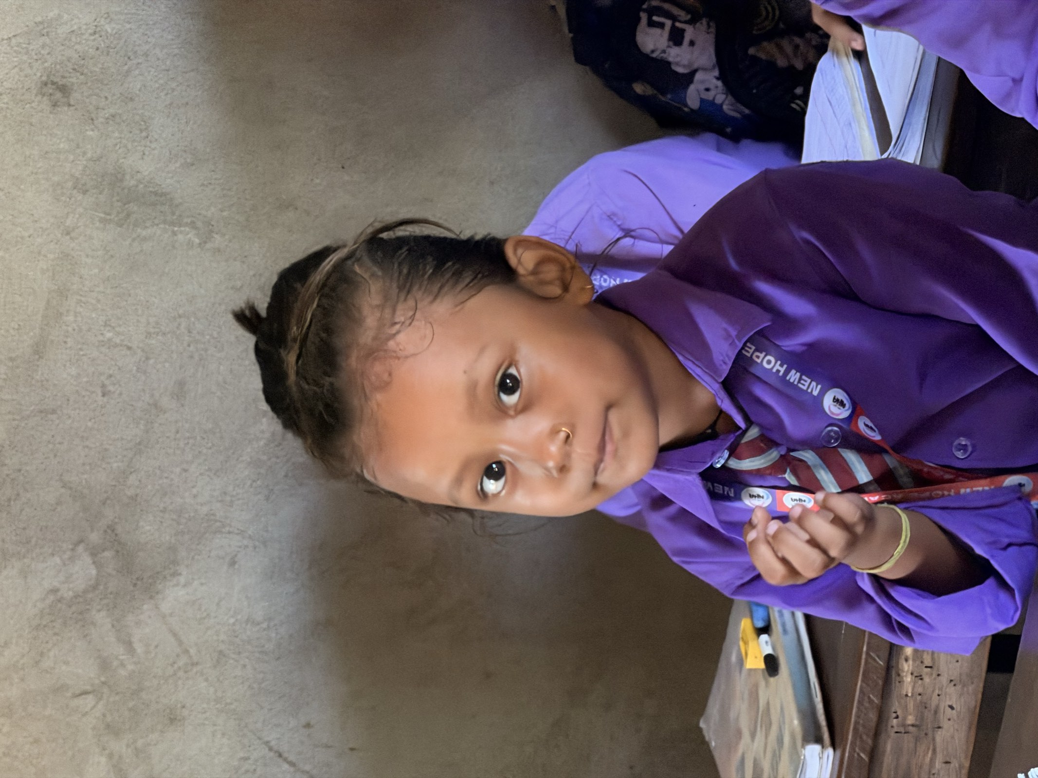 A young student in her purple uniform looking up from her desk