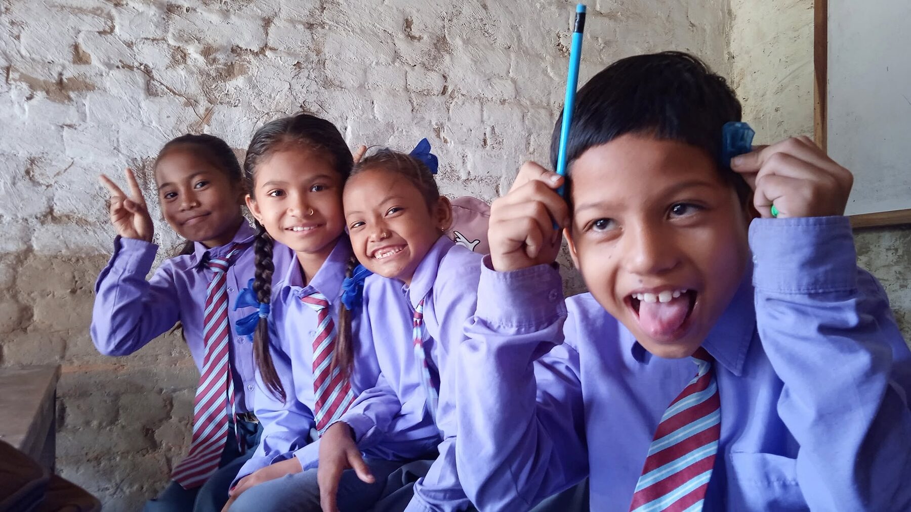 Smiling New Hope Academy students raising their pencils together