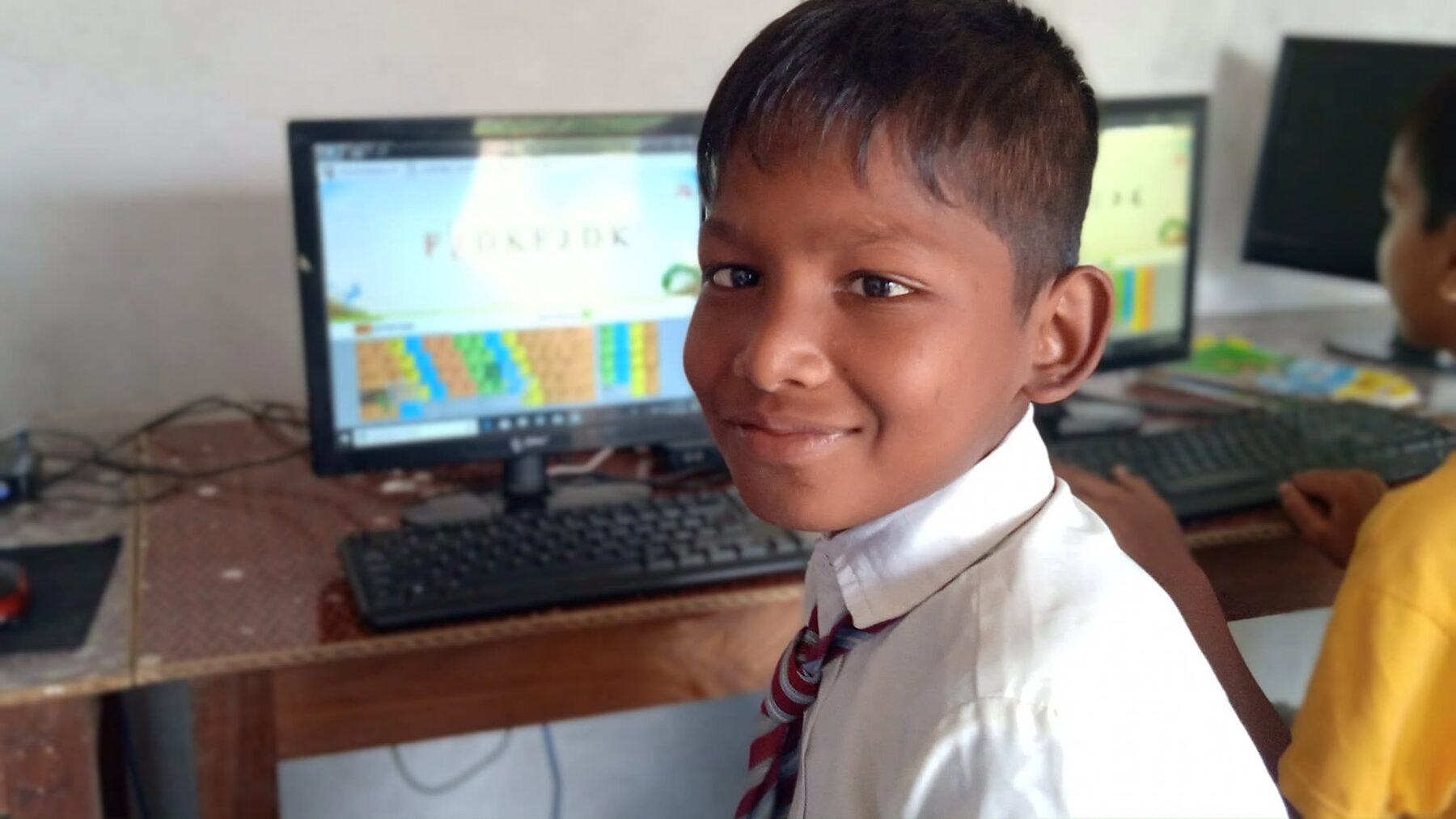 A young student proudly seated at a computer in the school lab