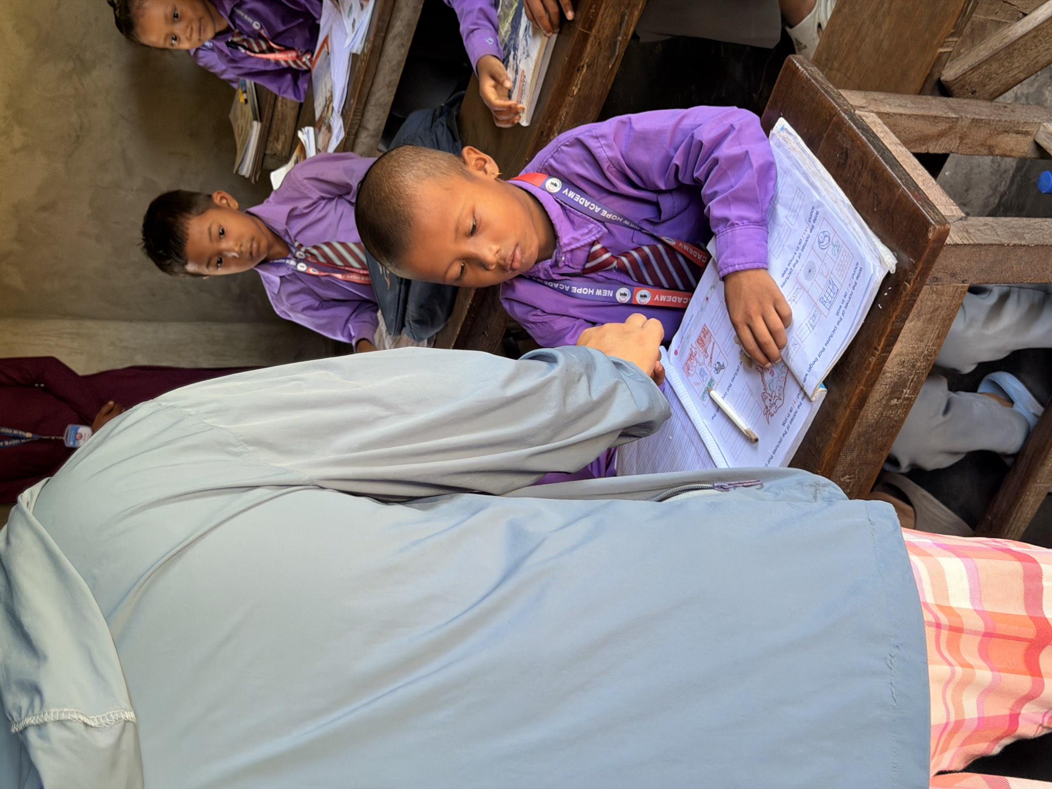 A teacher bending over a desk to help a young student with his workbook